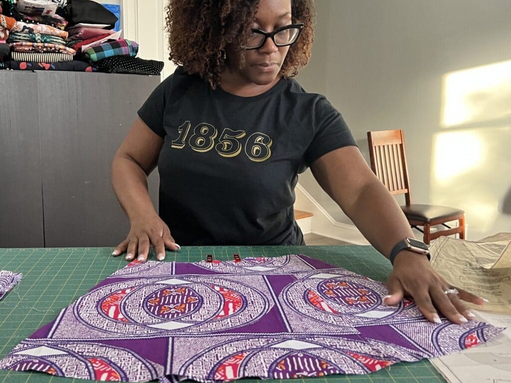 black girl with glasses lays out and organizing purple ankara fabric