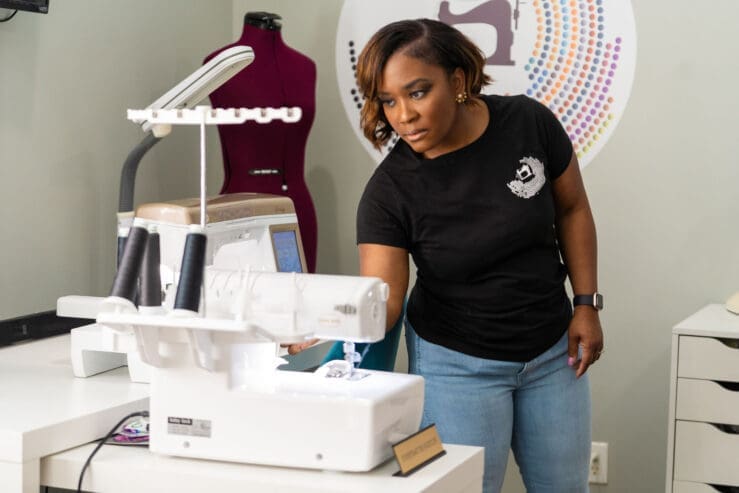 Shontae Buffington, an African American woman turns on her Babylock Serger in her sewing space