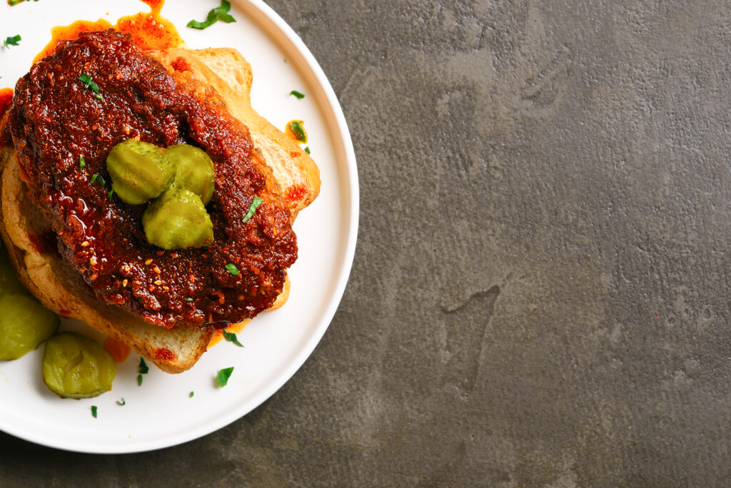 Nashville hot chicken sandwich on plate over brown background with free text space. Top view, flat lay